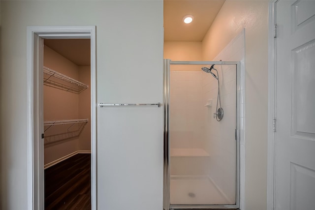 bathroom featuring a shower stall, a walk in closet, and wood finished floors