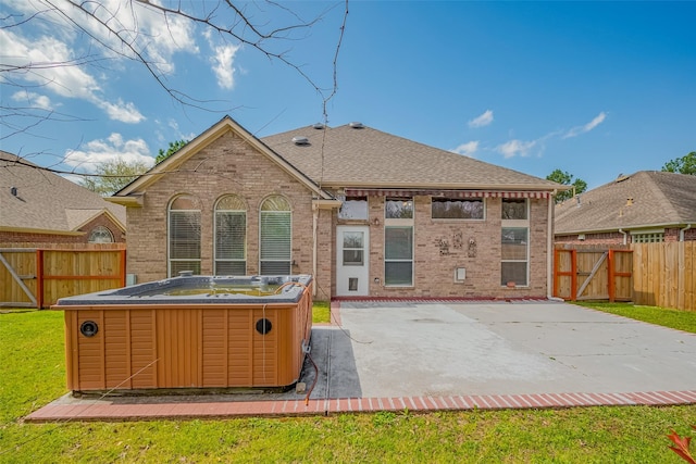 rear view of property featuring brick siding, a fenced backyard, a hot tub, and a patio