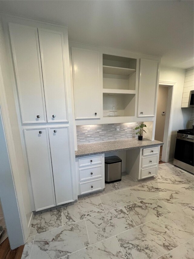 kitchen featuring white cabinets, built in desk, backsplash, and gas stove