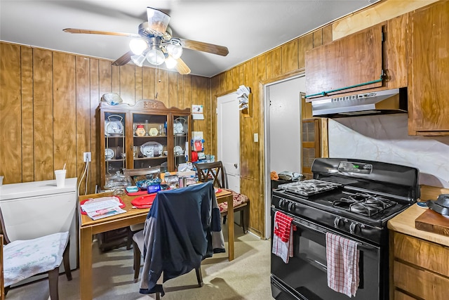 kitchen featuring ceiling fan, light carpet, gas stove, and wooden walls