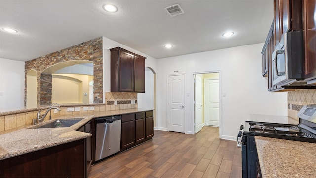 kitchen with stainless steel appliances, sink, light stone counters, backsplash, and dark hardwood / wood-style floors