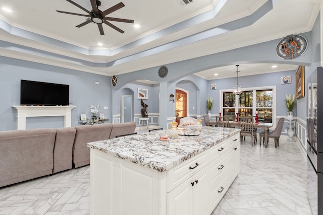 kitchen with ceiling fan with notable chandelier, white cabinets, a center island, hanging light fixtures, and a raised ceiling