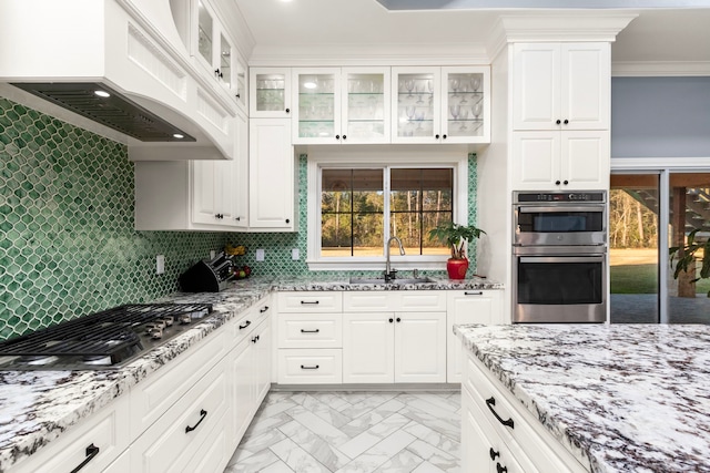 kitchen with light stone countertops, white cabinets, appliances with stainless steel finishes, custom exhaust hood, and sink