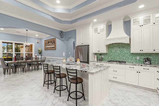 kitchen featuring white cabinets, appliances with stainless steel finishes, a center island, wall chimney exhaust hood, and a raised ceiling