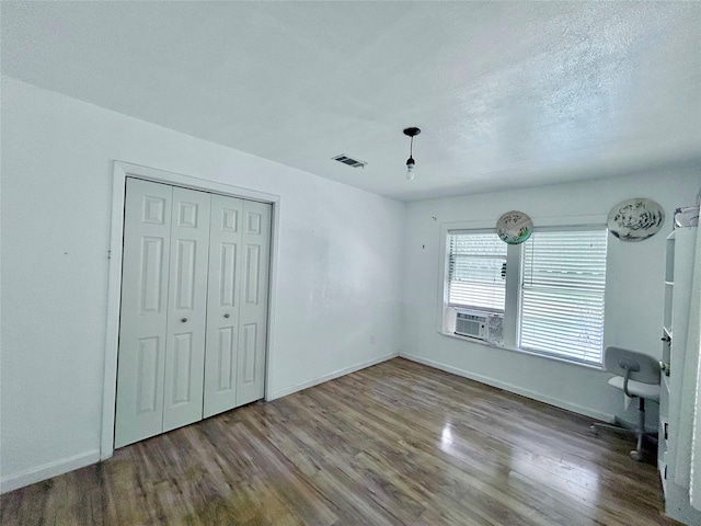 unfurnished bedroom with a textured ceiling, cooling unit, a closet, and wood-type flooring