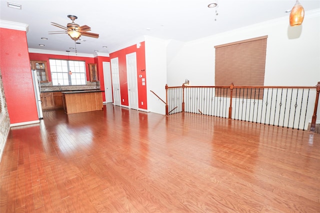 unfurnished living room featuring ceiling fan, crown molding, sink, and hardwood / wood-style flooring