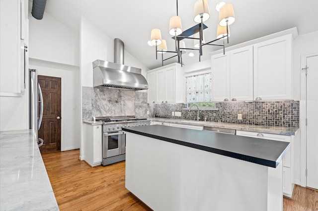 kitchen featuring hanging light fixtures, stainless steel appliances, wall chimney range hood, white cabinetry, and sink