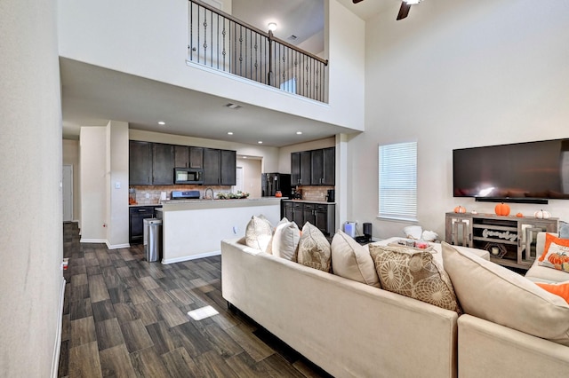 living room featuring a towering ceiling, ceiling fan, and dark wood-type flooring