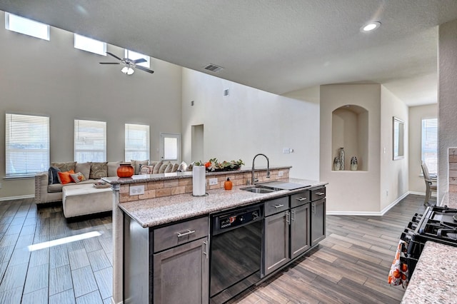 kitchen featuring sink, dark brown cabinetry, light stone countertops, a center island with sink, and black appliances