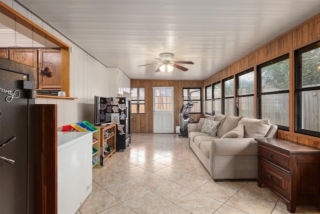 living room with light tile patterned floors, ceiling fan, and wood walls