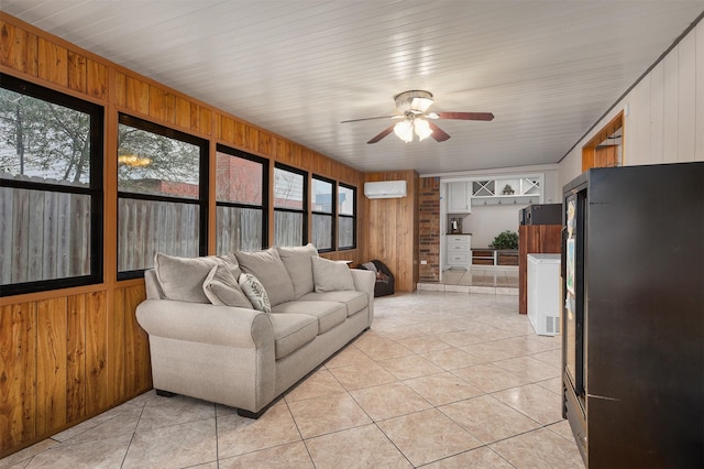 living room with light tile patterned flooring, ceiling fan, a wall unit AC, and wood walls