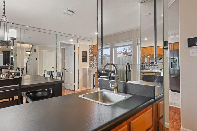 kitchen with pendant lighting, sink, crown molding, tasteful backsplash, and stainless steel fridge with ice dispenser