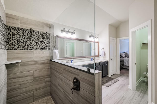 bathroom with tiled shower, vanity, and vaulted ceiling