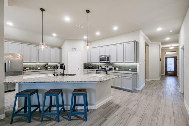 kitchen featuring decorative light fixtures, sink, appliances with stainless steel finishes, and a kitchen island with sink