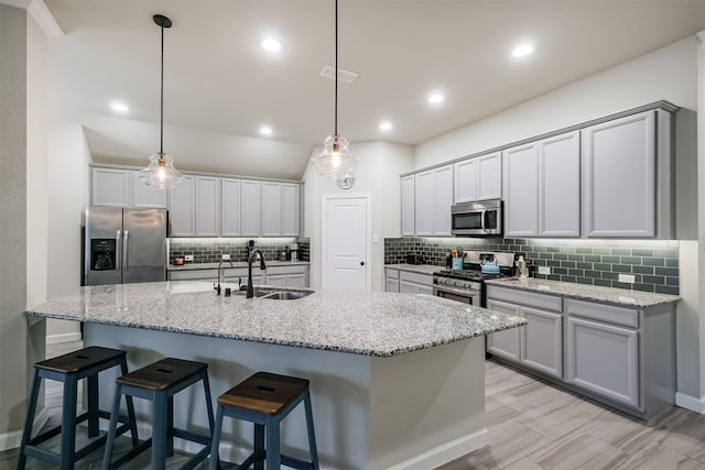 kitchen with appliances with stainless steel finishes, an island with sink, hanging light fixtures, and sink