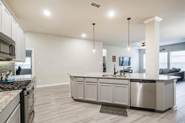 kitchen with white cabinetry, stainless steel appliances, an island with sink, sink, and hanging light fixtures