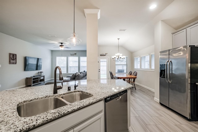 kitchen with appliances with stainless steel finishes, hanging light fixtures, light stone countertops, ceiling fan with notable chandelier, and sink