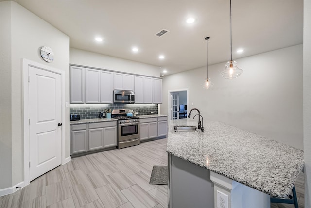 kitchen with decorative light fixtures, stainless steel appliances, tasteful backsplash, an island with sink, and sink