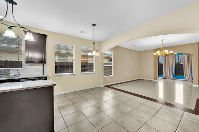 kitchen with a notable chandelier, light tile patterned flooring, dark brown cabinetry, hanging light fixtures, and light stone counters