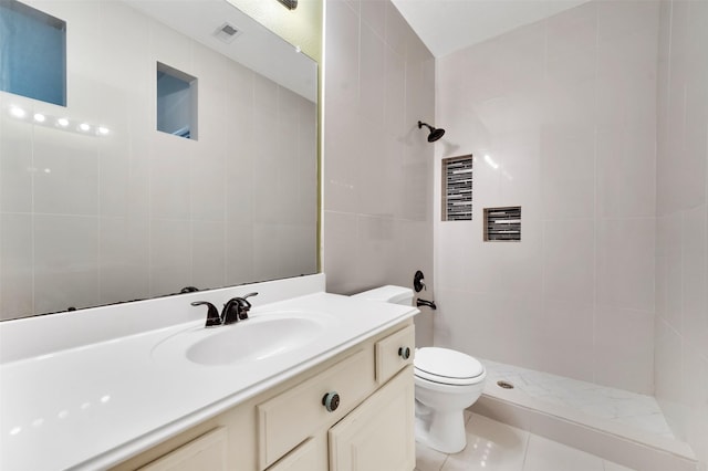 bathroom featuring toilet, vanity, tile walls, tile patterned flooring, and a tile shower