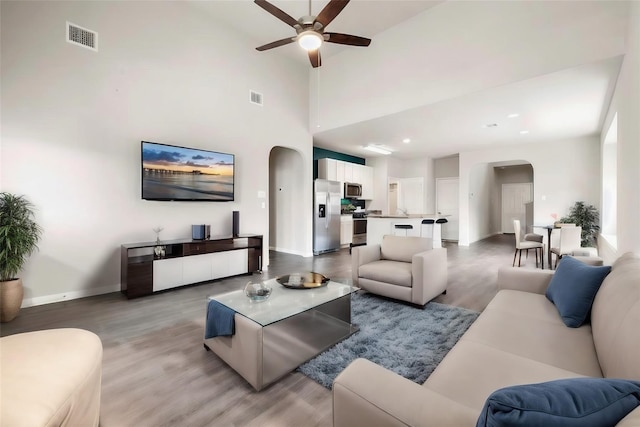 living room featuring a towering ceiling, ceiling fan, and light wood-type flooring