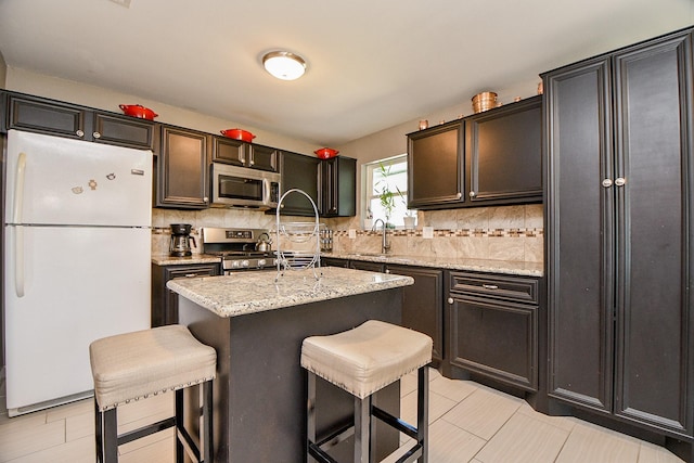 kitchen featuring sink, a center island, light stone countertops, a breakfast bar, and appliances with stainless steel finishes