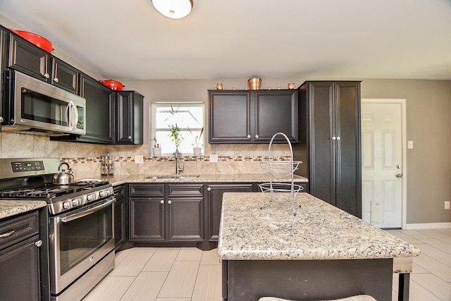 kitchen with sink, light stone counters, decorative backsplash, a kitchen island, and appliances with stainless steel finishes