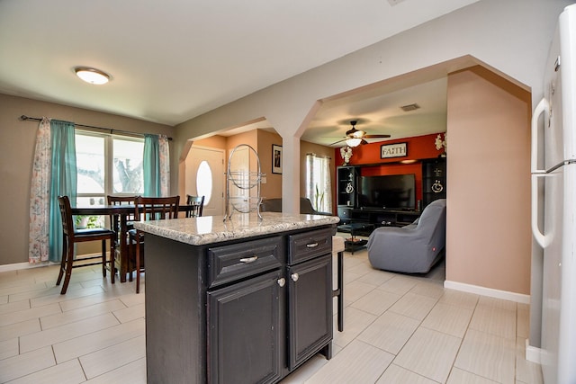 kitchen featuring white refrigerator, a kitchen island, ceiling fan, and light stone countertops