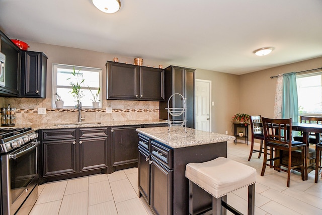 kitchen featuring light stone counters, a center island, backsplash, and stainless steel gas range oven