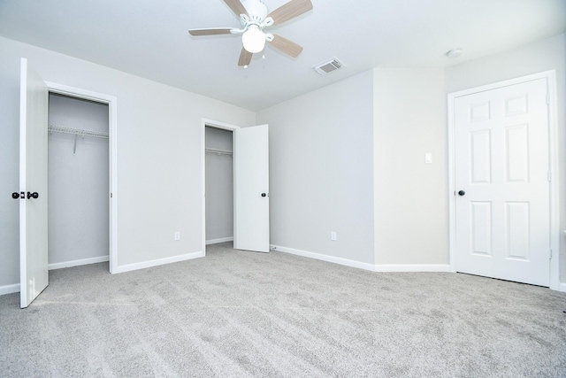 unfurnished bedroom with two closets, ceiling fan, and light colored carpet