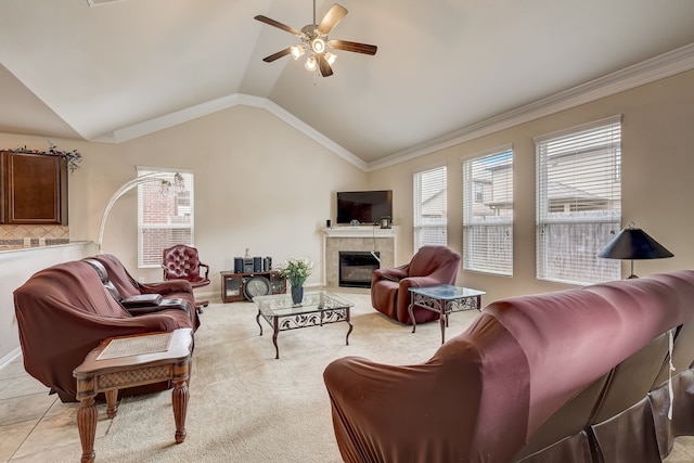 carpeted living room with ceiling fan, ornamental molding, a tiled fireplace, and vaulted ceiling