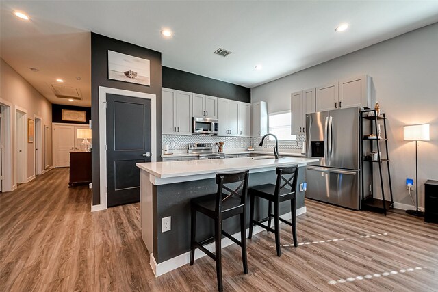 kitchen with stainless steel appliances, light hardwood / wood-style floors, a kitchen island with sink, a breakfast bar area, and white cabinets