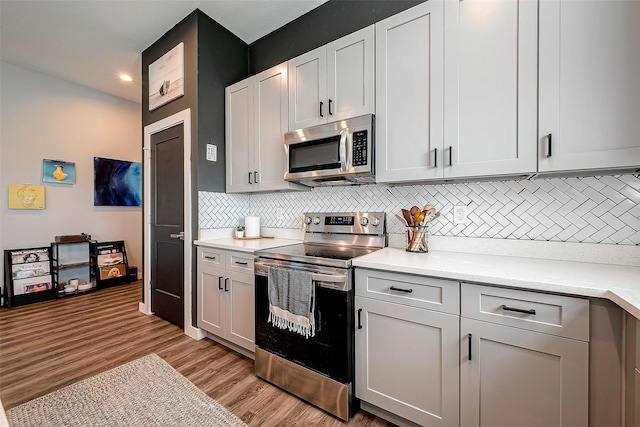 kitchen featuring appliances with stainless steel finishes, light wood-type flooring, light stone countertops, white cabinets, and backsplash