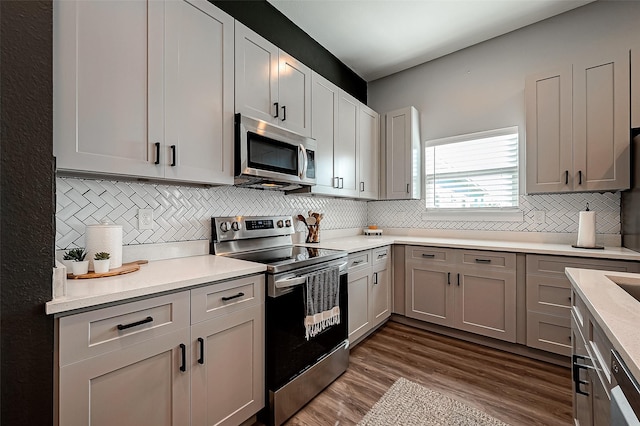 kitchen with stainless steel appliances, gray cabinets, tasteful backsplash, and dark wood-type flooring