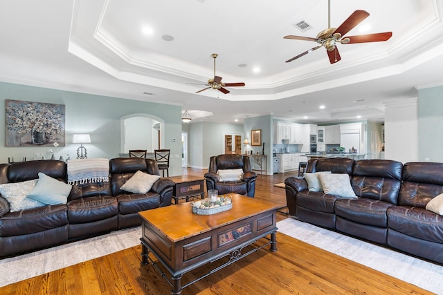 living room featuring a tray ceiling, crown molding, and light hardwood / wood-style floors