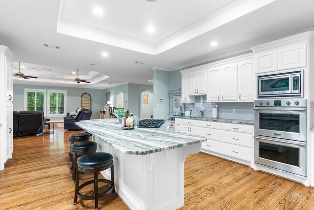 kitchen featuring white cabinets, a raised ceiling, light wood-type flooring, light stone countertops, and appliances with stainless steel finishes