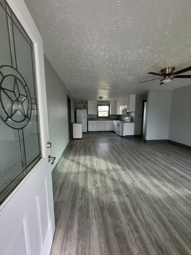 unfurnished living room with ceiling fan, a textured ceiling, and dark hardwood / wood-style flooring