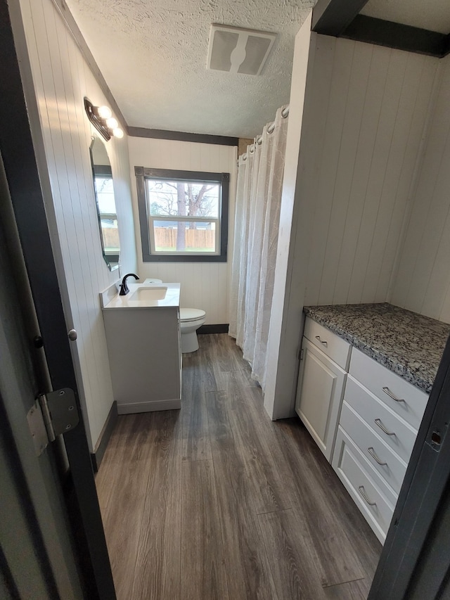 bathroom featuring toilet, vanity, wood walls, hardwood / wood-style flooring, and a textured ceiling