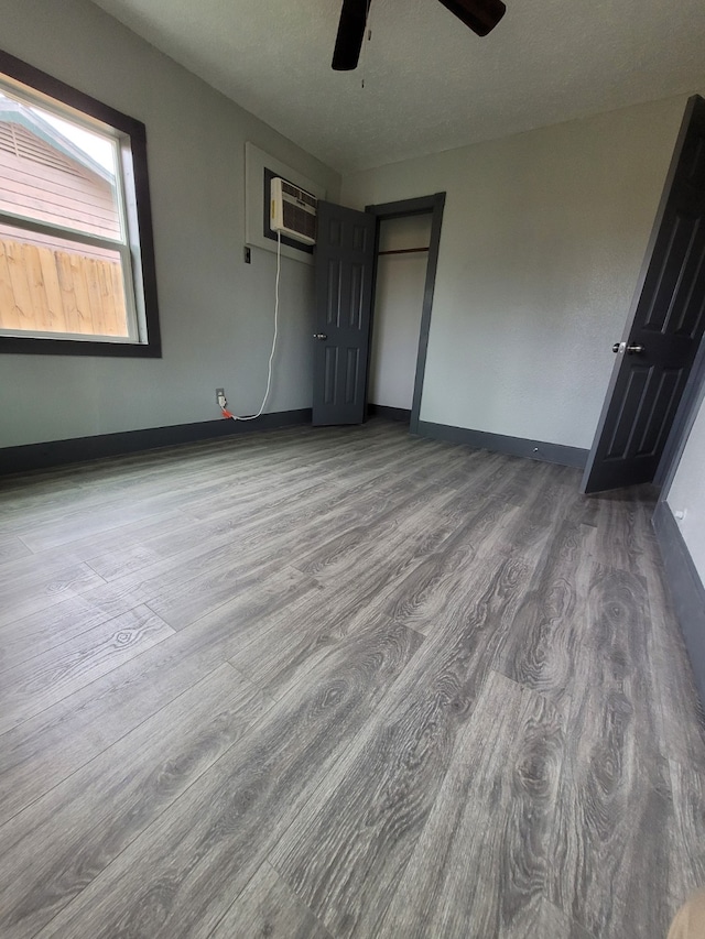 unfurnished bedroom featuring ceiling fan, an AC wall unit, and wood-type flooring