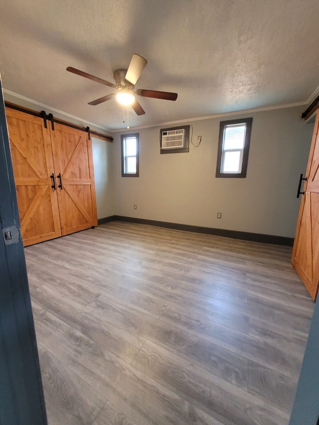 unfurnished bedroom featuring ceiling fan, a barn door, crown molding, a wall mounted air conditioner, and light wood-type flooring