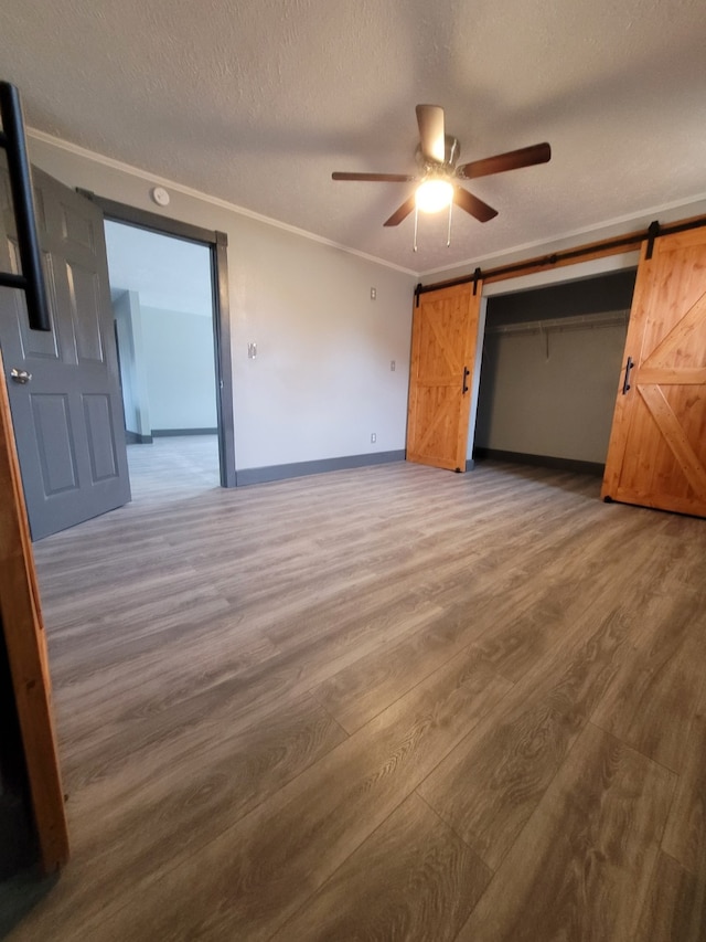 unfurnished bedroom with ceiling fan, a barn door, and hardwood / wood-style floors