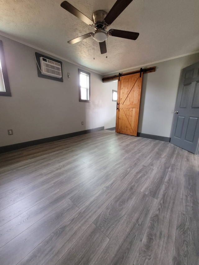 unfurnished room featuring a barn door, a wall unit AC, wood-type flooring, crown molding, and a textured ceiling