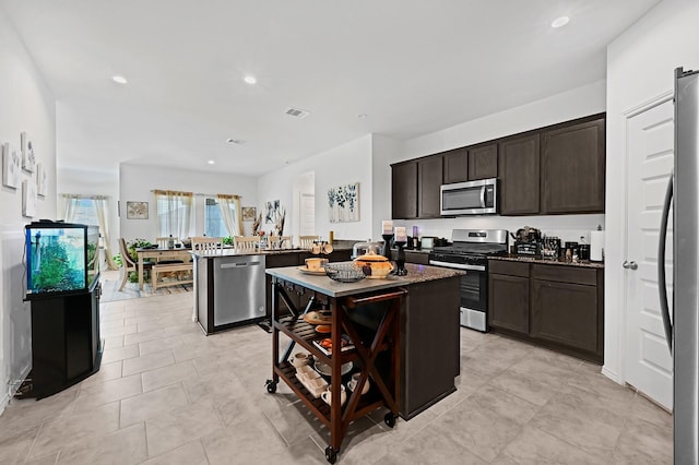 kitchen featuring light tile patterned floors, stainless steel appliances, dark brown cabinets, and a center island