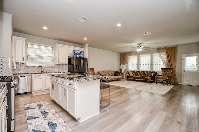 kitchen with appliances with stainless steel finishes, a center island, white cabinetry, dark stone counters, and a breakfast bar