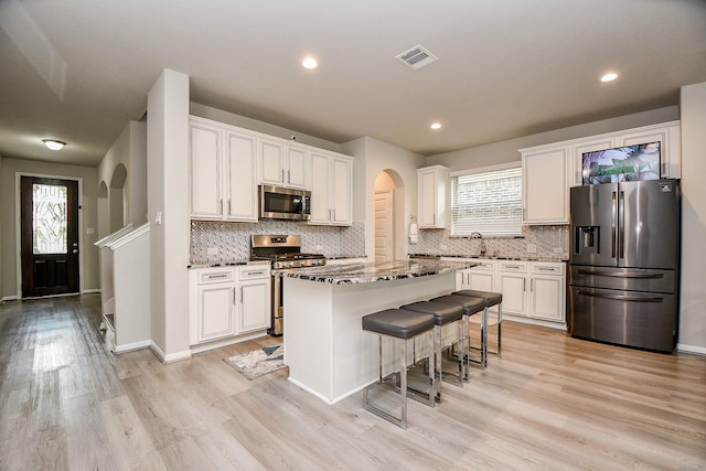 kitchen featuring white cabinetry, dark stone countertops, stainless steel appliances, and a kitchen island