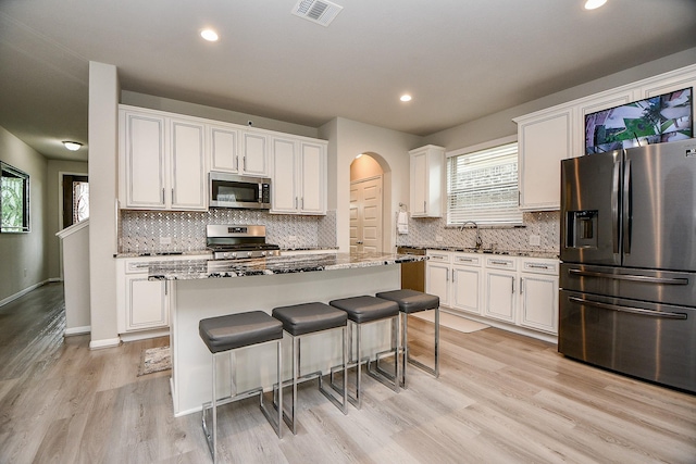 kitchen with white cabinets, light stone counters, stainless steel appliances, and a center island