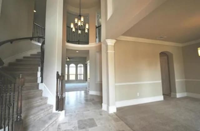 foyer entrance with ornamental molding, ceiling fan with notable chandelier, and decorative columns