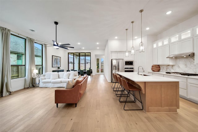 kitchen with white cabinetry, stainless steel appliances, an island with sink, decorative backsplash, and sink