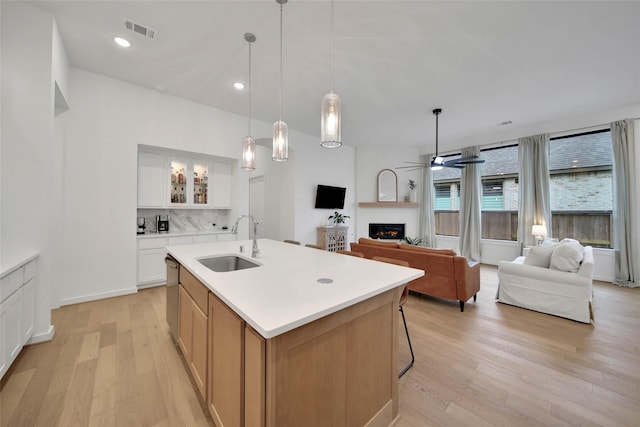 kitchen featuring decorative light fixtures, a center island with sink, stainless steel dishwasher, sink, and white cabinets