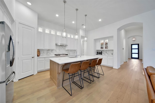 kitchen with white cabinetry, a center island with sink, stainless steel fridge, backsplash, and pendant lighting